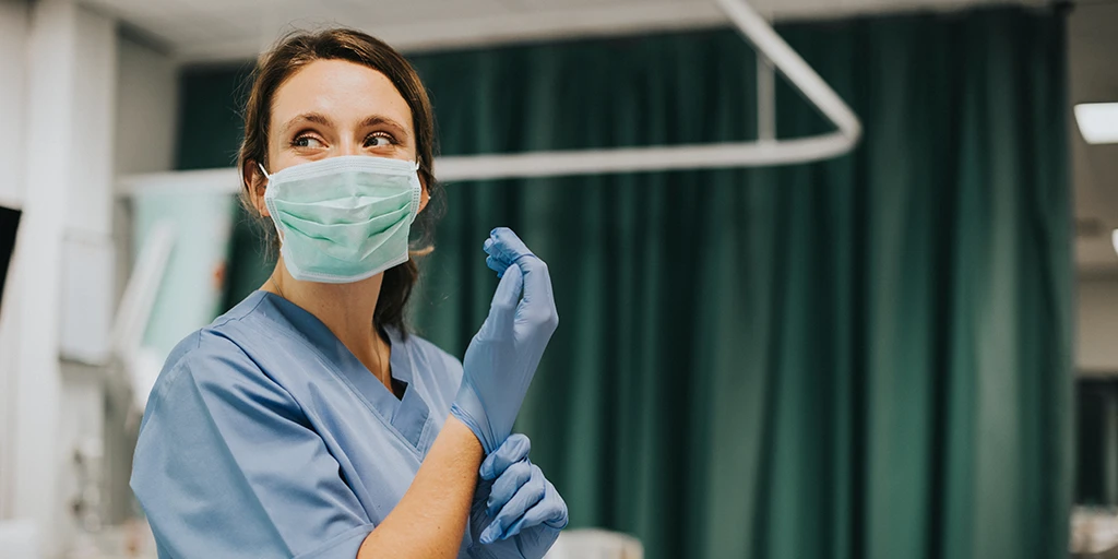 Nurse donning gloves while wearing scrubs and mask