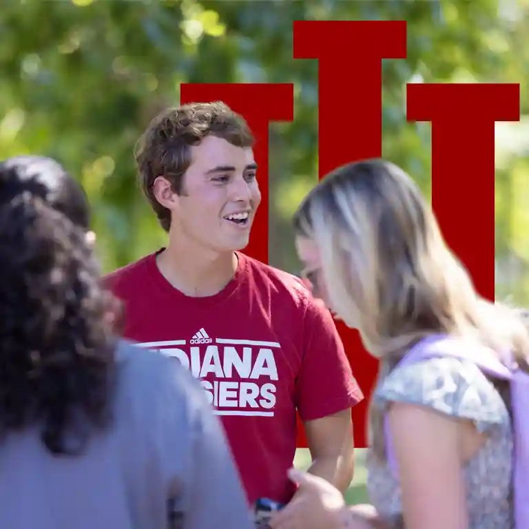 Male student wearing Indiana t-shirt smiling on campus with IU trident behind him