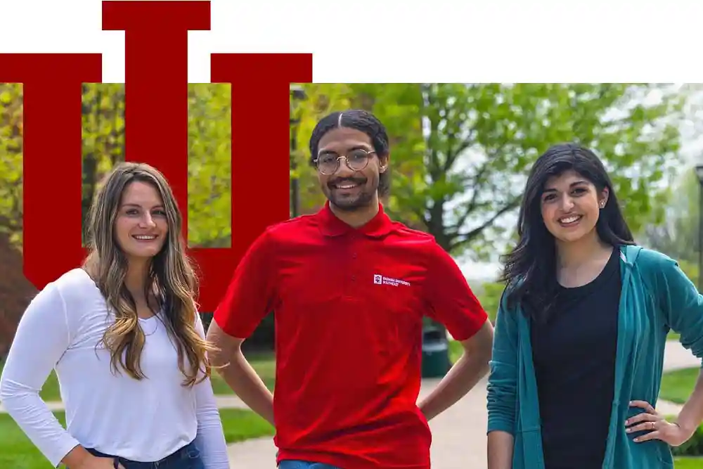 Three IU Southeast students smiling into camera with campus and IU trident behind them
