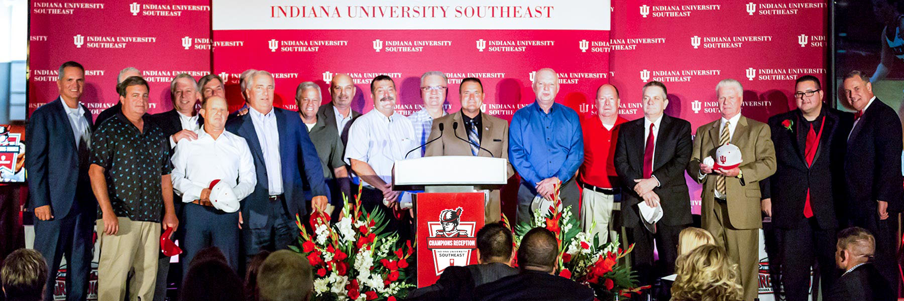 Group of men posing in front of an Indiana University Southeast background with a podium in the middle bearing the logo for the Champions Reception