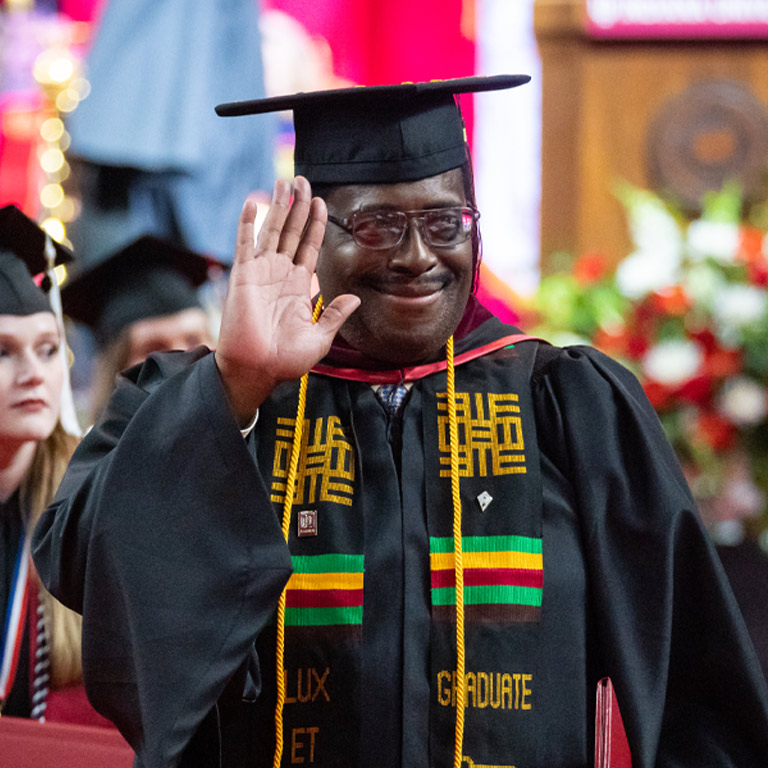 A graduate student waves to the crowd