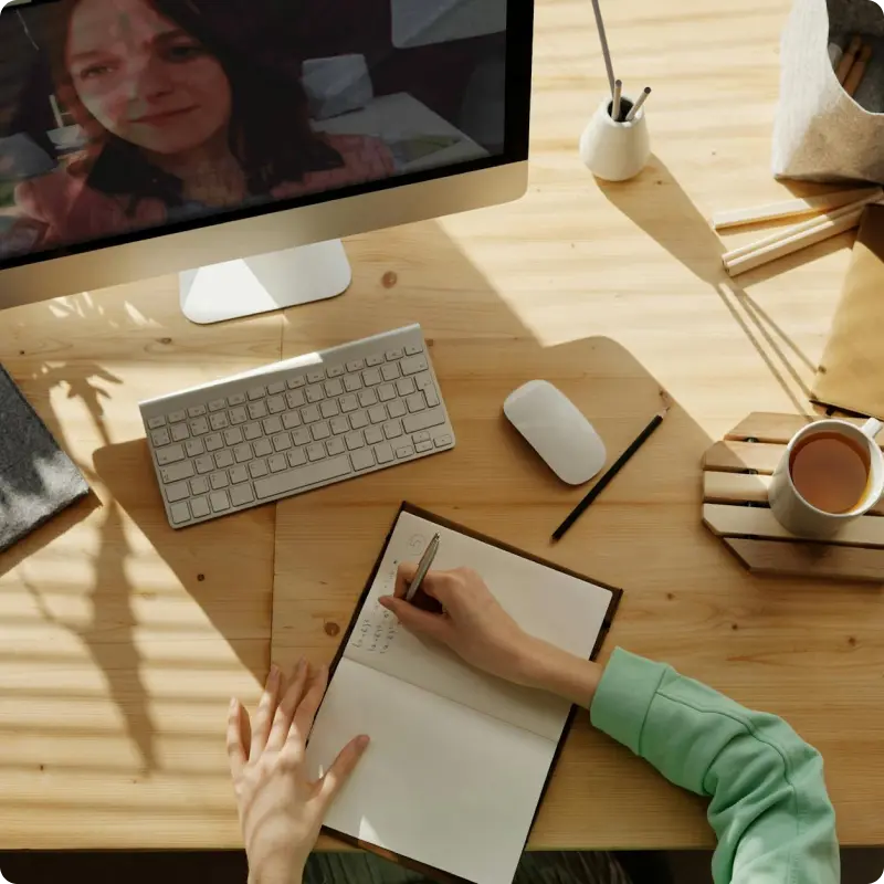 Person writing in a notebook at a desk with a computer