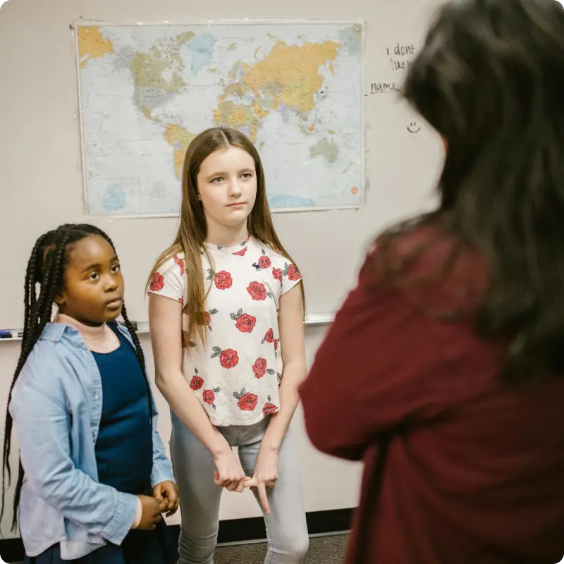 Two young students standing and listening to an adult