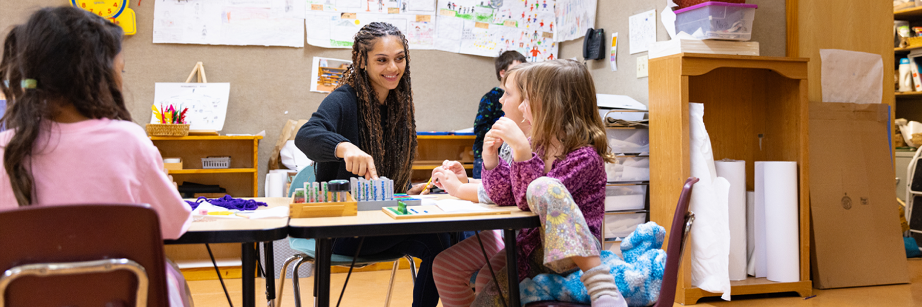 College-aged female teacher works with young students in a Montessori school.