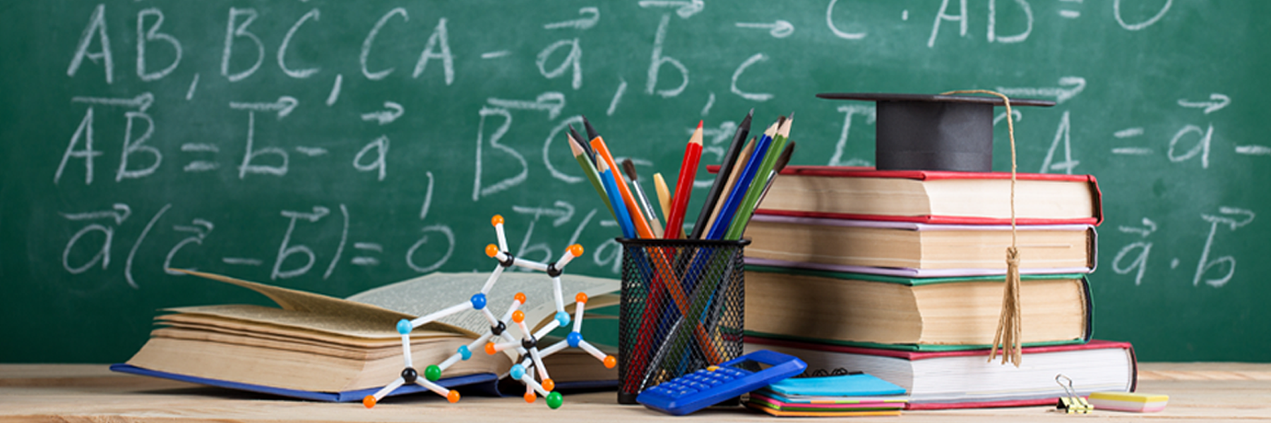 Books and other educational materials on a desk in front of a chalkboard containing mathematical equations.