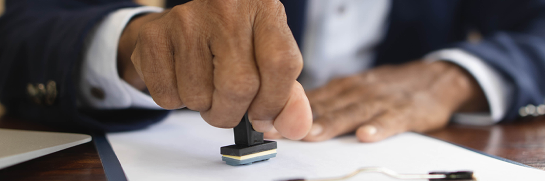 Close-up of a hand rubber-stamping a pile of papers.