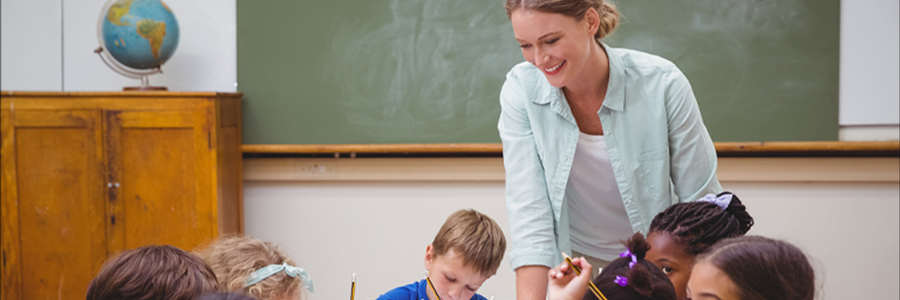 Female teacher working with elementary school students in a cluster of desks in classroom.