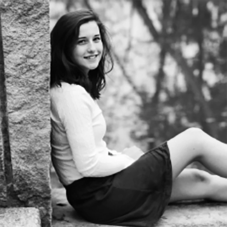 Black and white photo of Honors Program graduate Emily Kenney posing against a wall