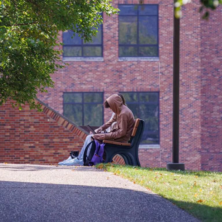 Students sitting outside on campus on a bench