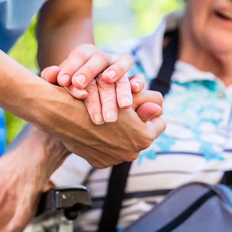 Nurse holding the hand of an elderly patient in a wheelchair