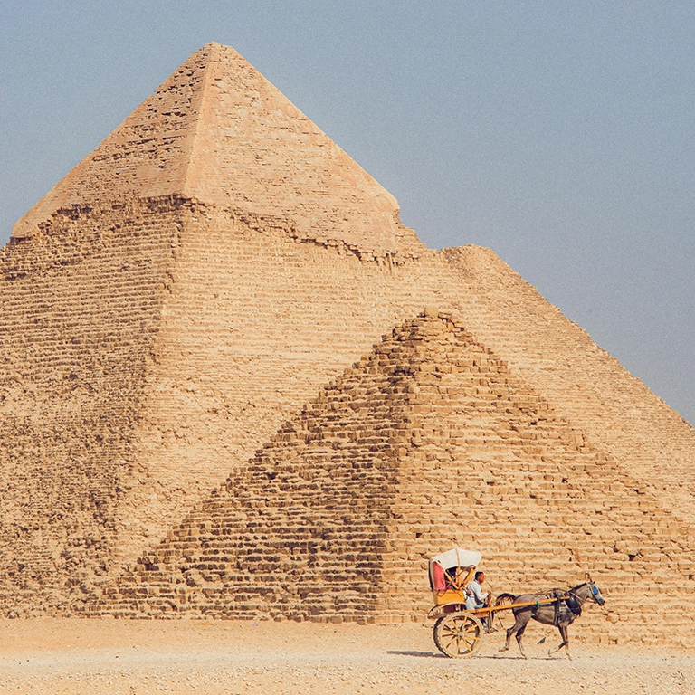 Egyptian pyramids on a sunny day with a horse and cart in front of it. 