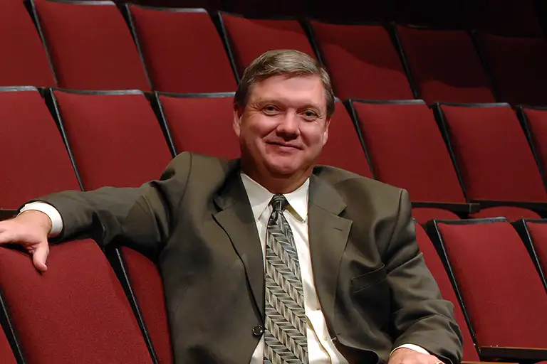 Former Ogle Center manager Kyle Ridout sitting in a red theater seat with an arm draped over the back and smiling